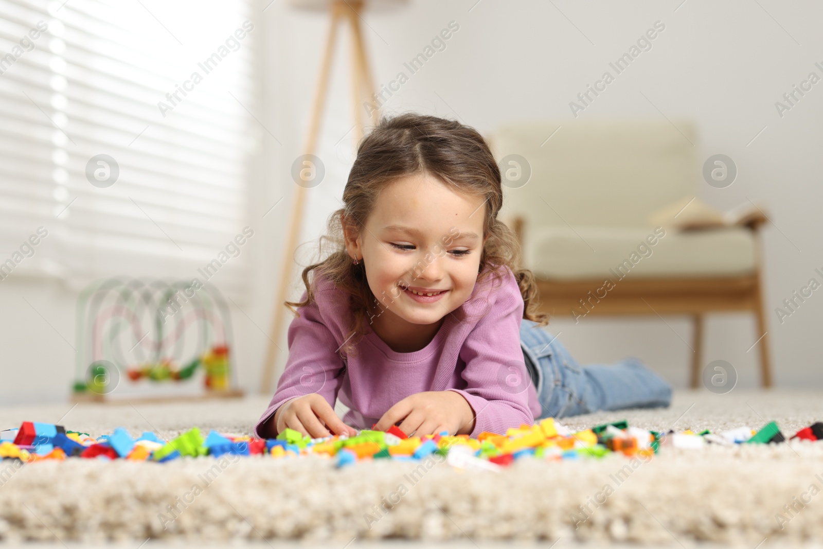 Photo of Cute girl playing with building blocks on floor at home