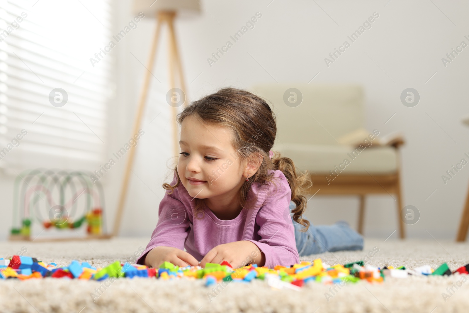 Photo of Cute girl playing with building blocks on floor at home