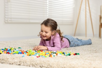 Photo of Cute girl playing with building blocks on floor at home