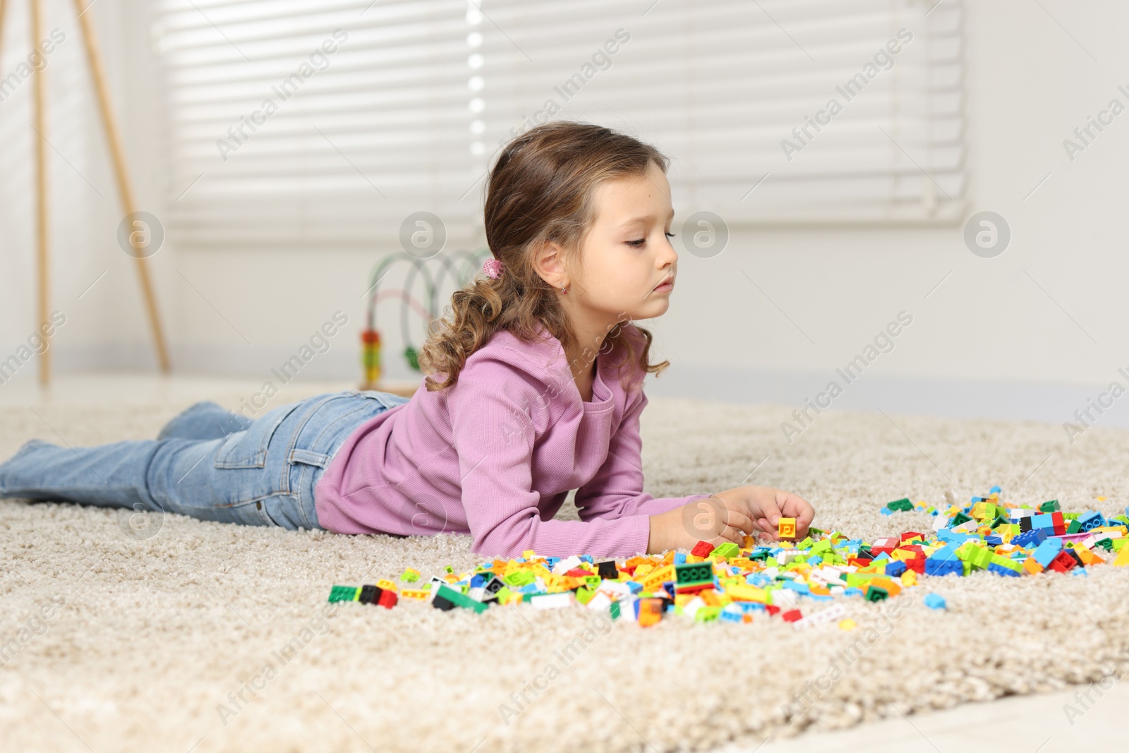 Photo of Cute girl playing with building blocks on floor at home