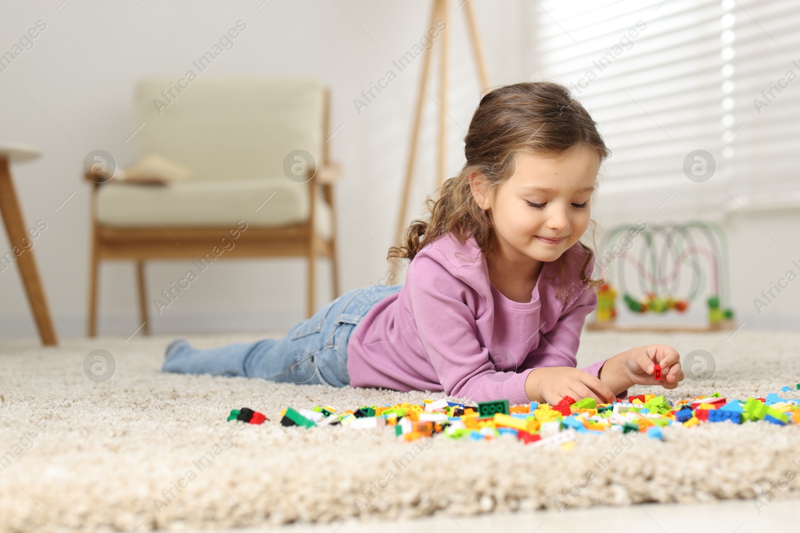 Photo of Cute girl playing with building blocks on floor at home