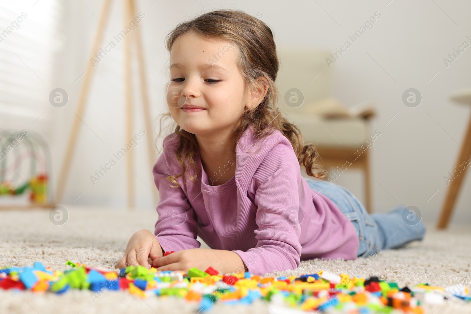 Photo of Cute girl playing with building blocks on floor at home