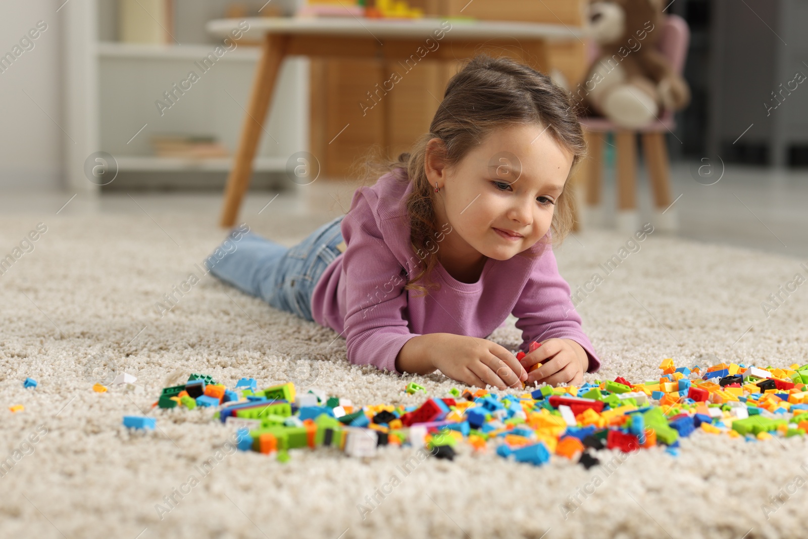 Photo of Cute girl playing with building blocks on floor at home