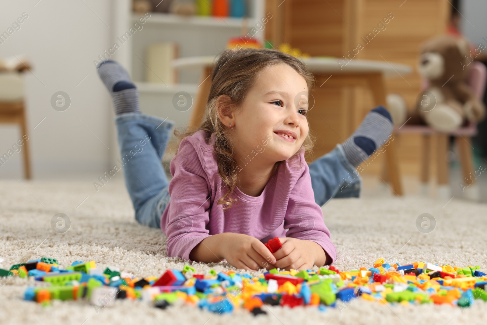 Photo of Cute girl playing with building blocks on floor at home