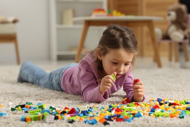 Photo of Cute girl playing with building blocks on floor at home