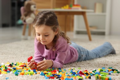 Photo of Cute girl playing with building blocks on floor at home