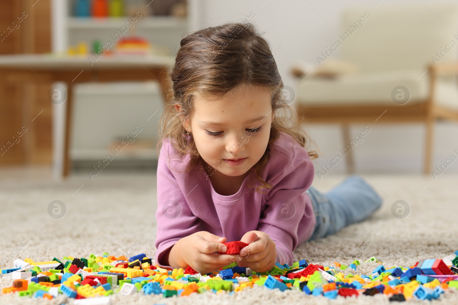 Photo of Cute girl playing with building blocks on floor at home