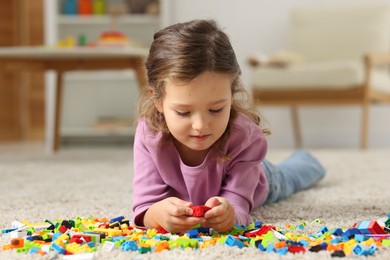 Photo of Cute girl playing with building blocks on floor at home