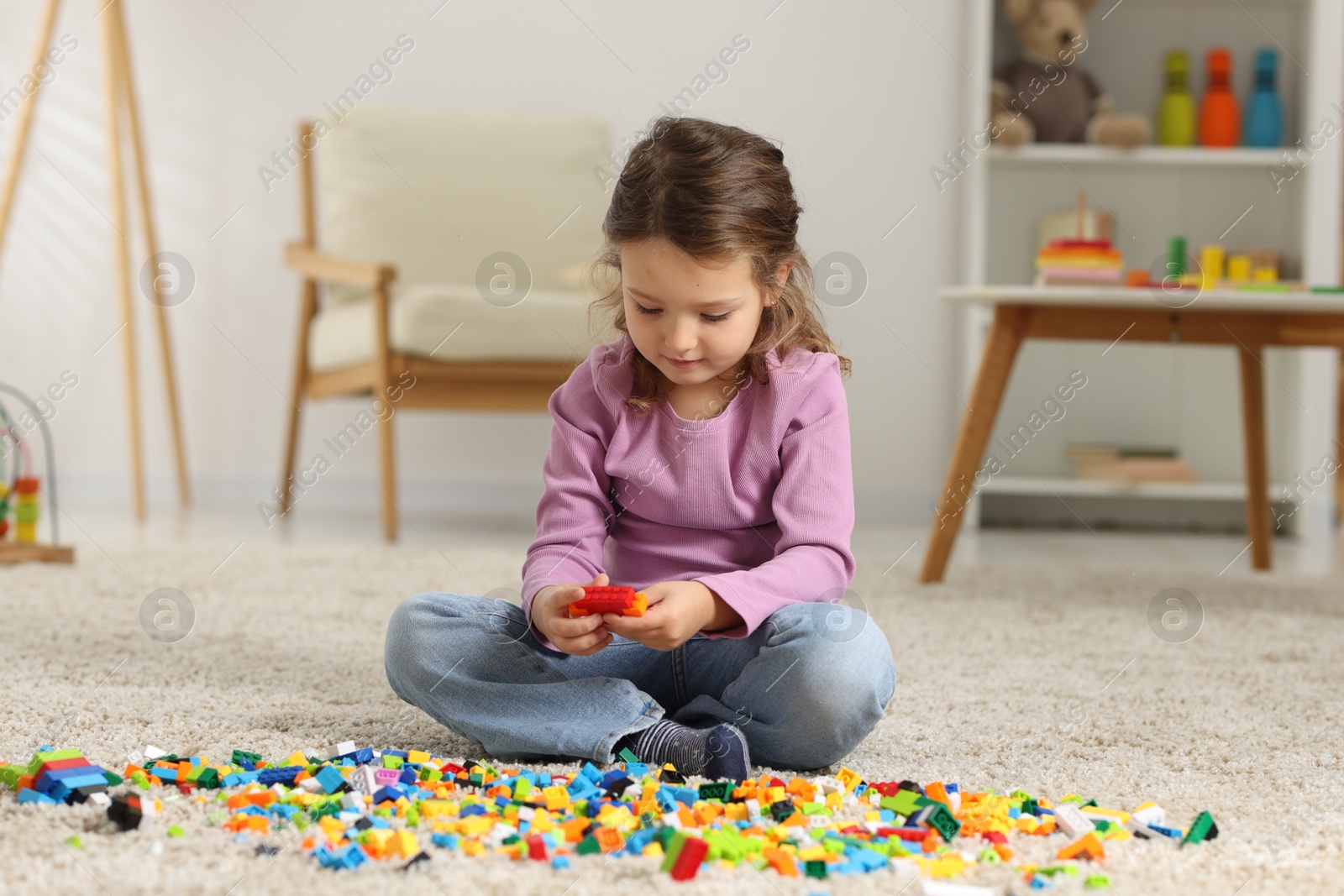 Photo of Cute girl playing with building blocks on floor at home