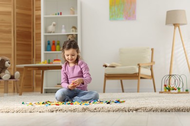 Photo of Cute girl playing with building blocks on floor at home. Space for text