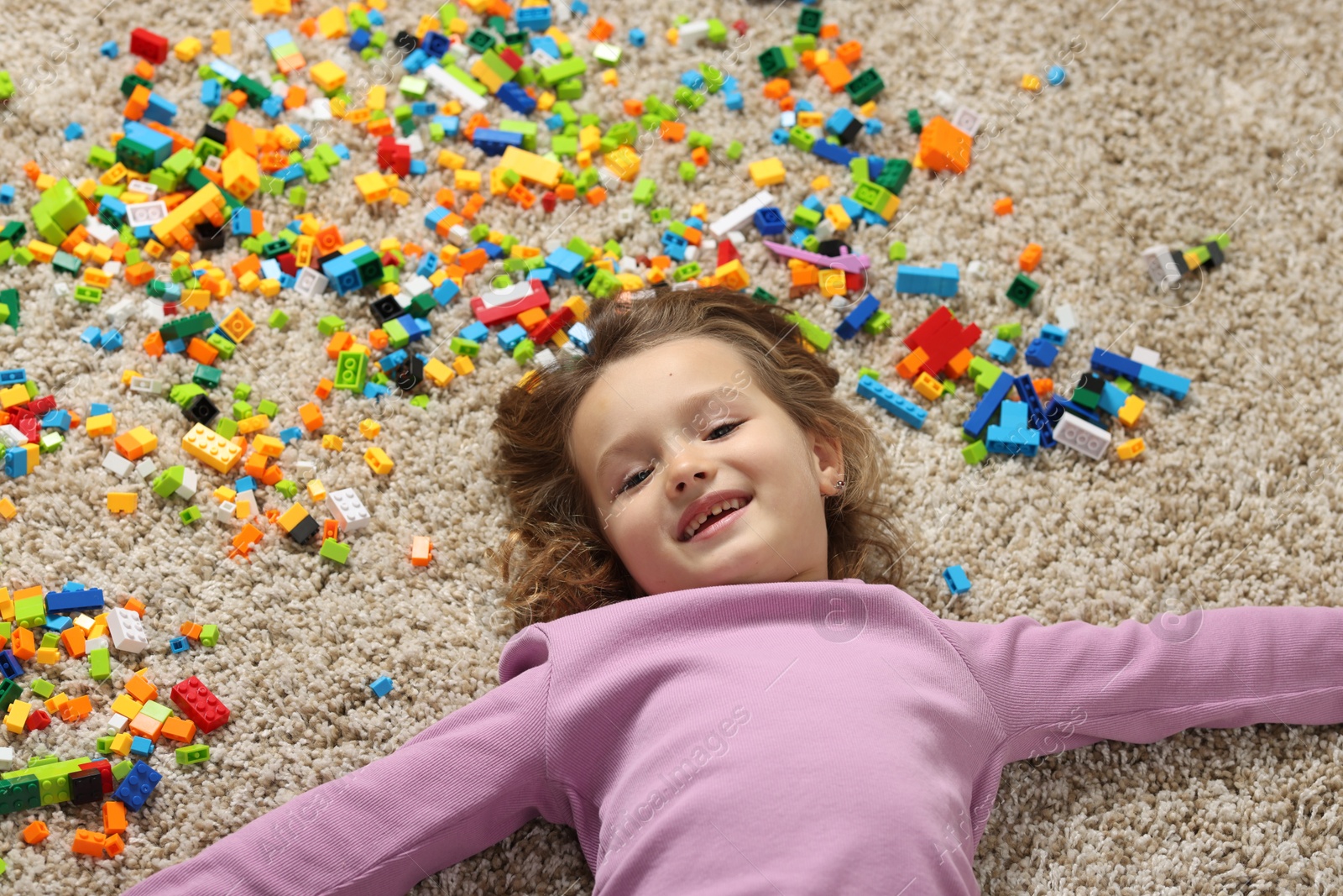 Photo of Cute girl lying near building blocks on carpet at home