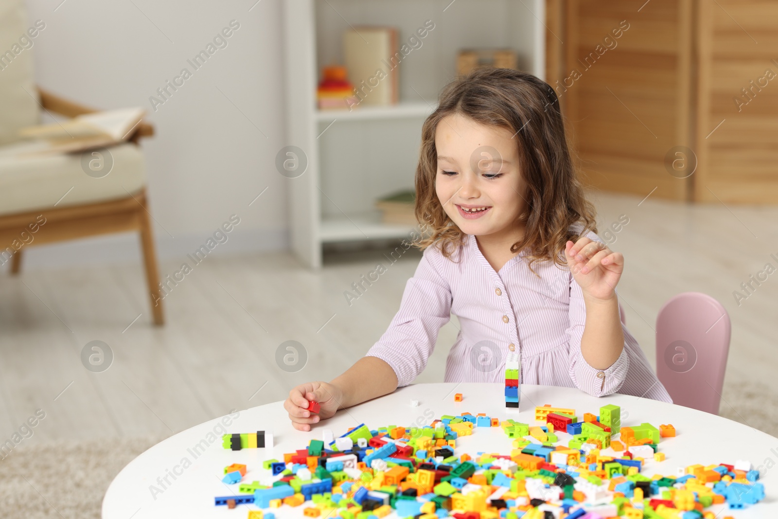 Photo of Cute girl playing with building blocks at white table indoors. Space for text