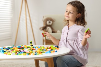 Photo of Cute girl playing with building blocks at white table indoors