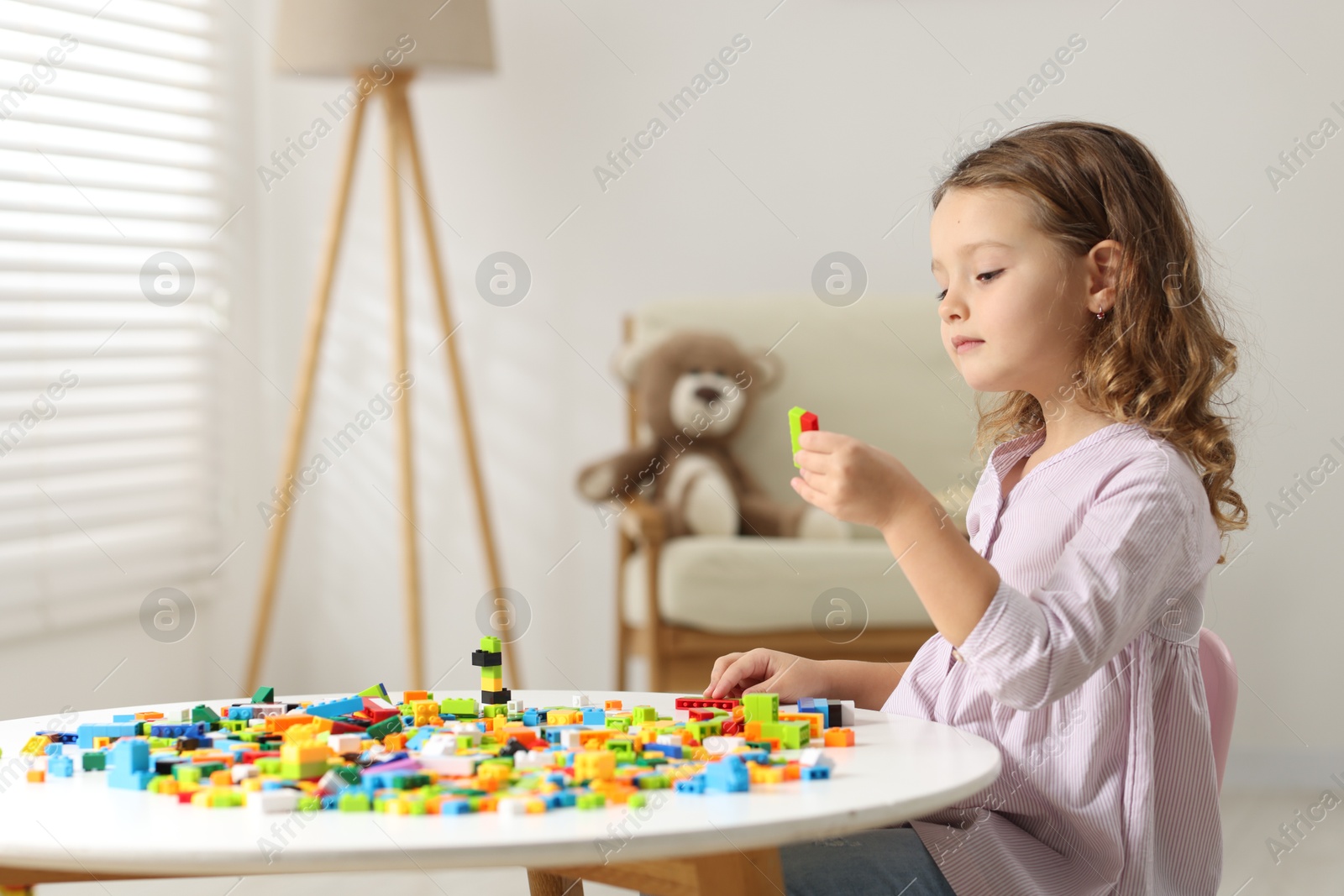 Photo of Cute girl playing with building blocks at white table indoors