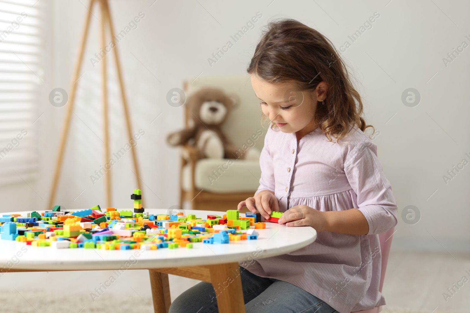 Photo of Cute girl playing with building blocks at white table indoors