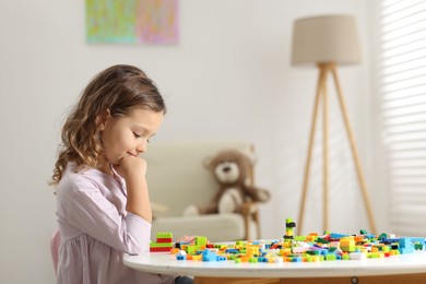 Photo of Cute girl playing with building blocks at white table indoors