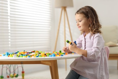 Photo of Cute girl playing with building blocks at white table indoors