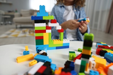 Photo of Girl playing with building blocks at white table indoors, closeup