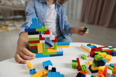 Photo of Girl playing with building blocks at white table indoors, closeup. Selective focus