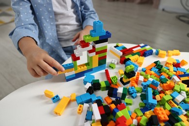 Photo of Girl playing with building blocks at white table indoors, closeup