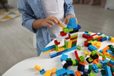 Photo of Girl playing with building blocks at white table indoors, closeup