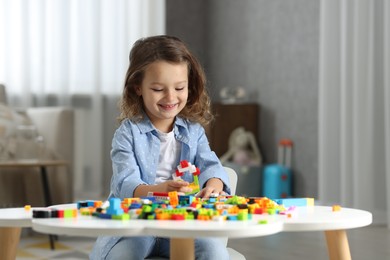 Photo of Cute girl playing with building blocks at white table indoors