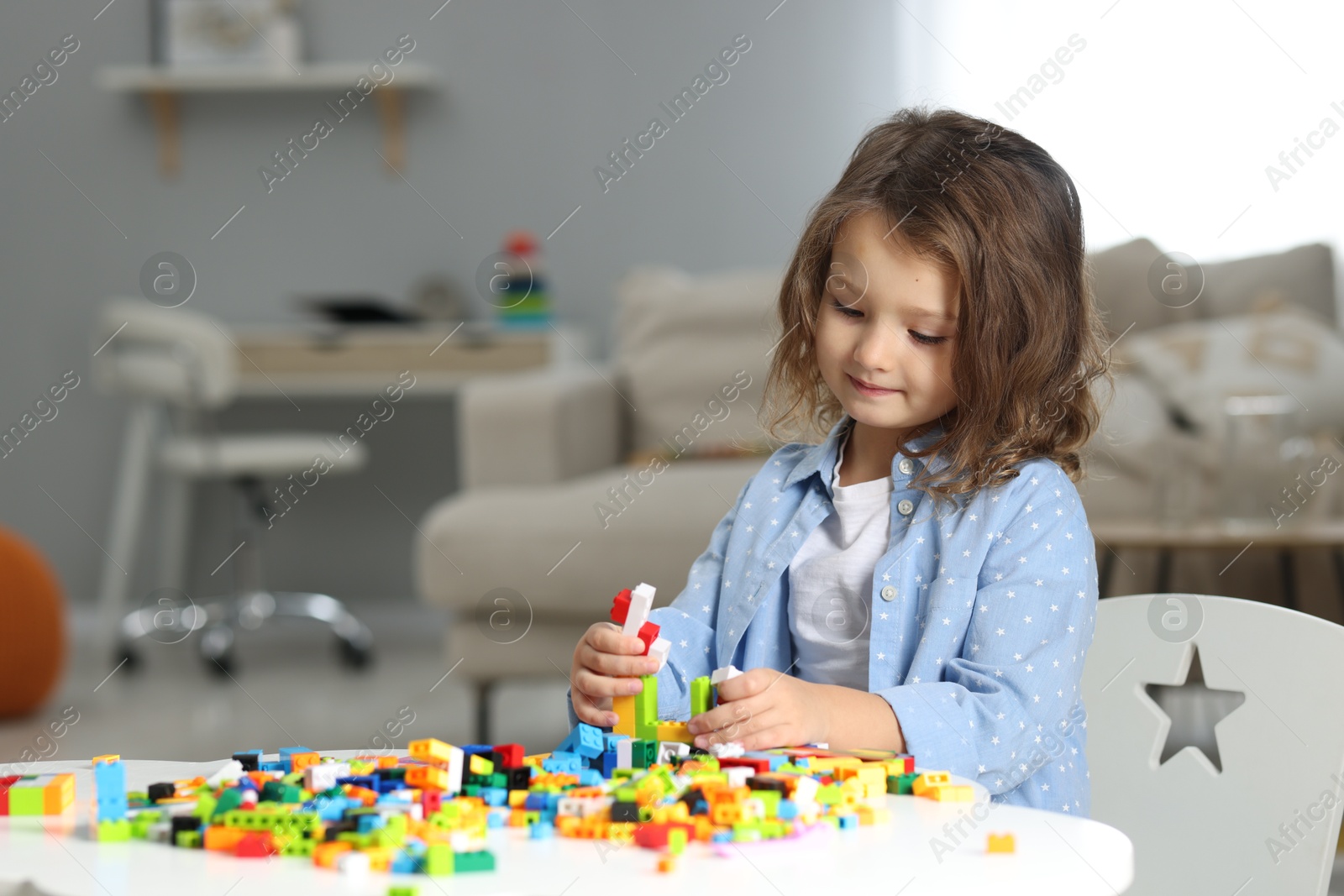 Photo of Cute girl playing with building blocks at white table indoors