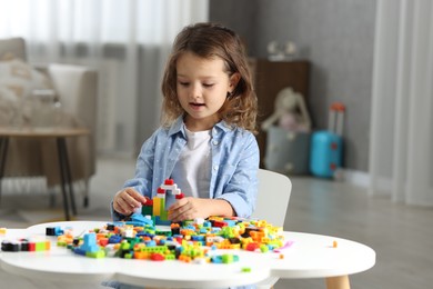 Photo of Cute girl playing with building blocks at white table indoors