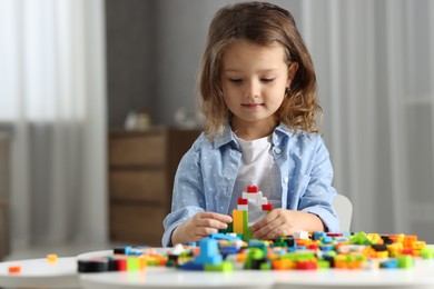 Photo of Cute girl playing with building blocks at white table indoors