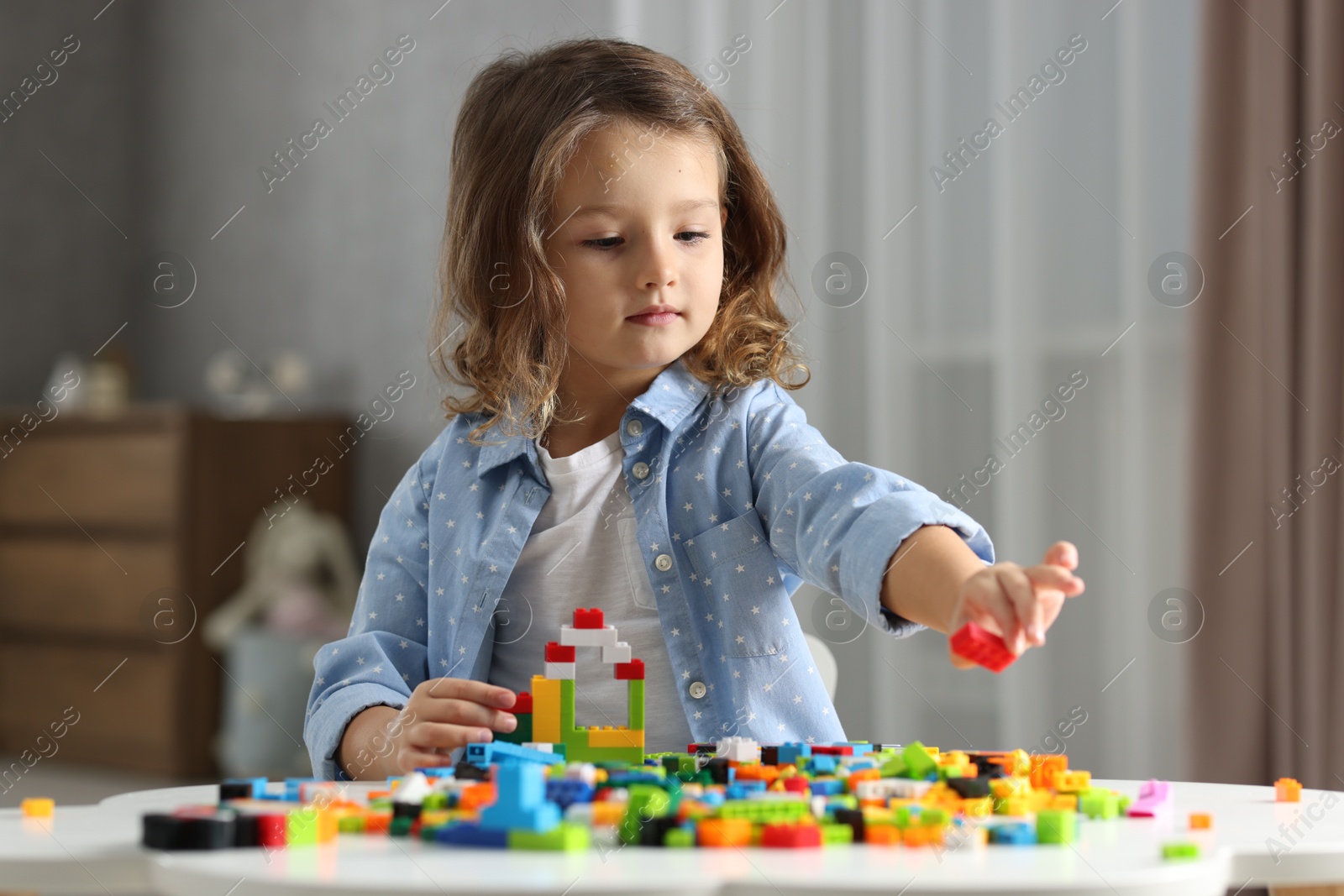 Photo of Cute girl playing with building blocks at white table indoors