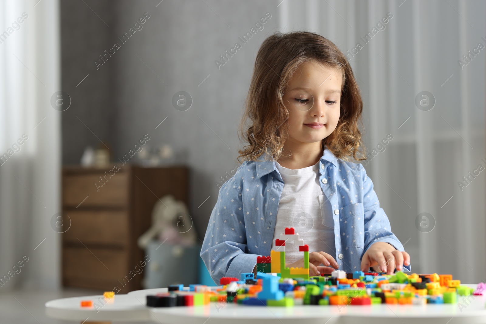 Photo of Cute girl playing with building blocks at white table indoors