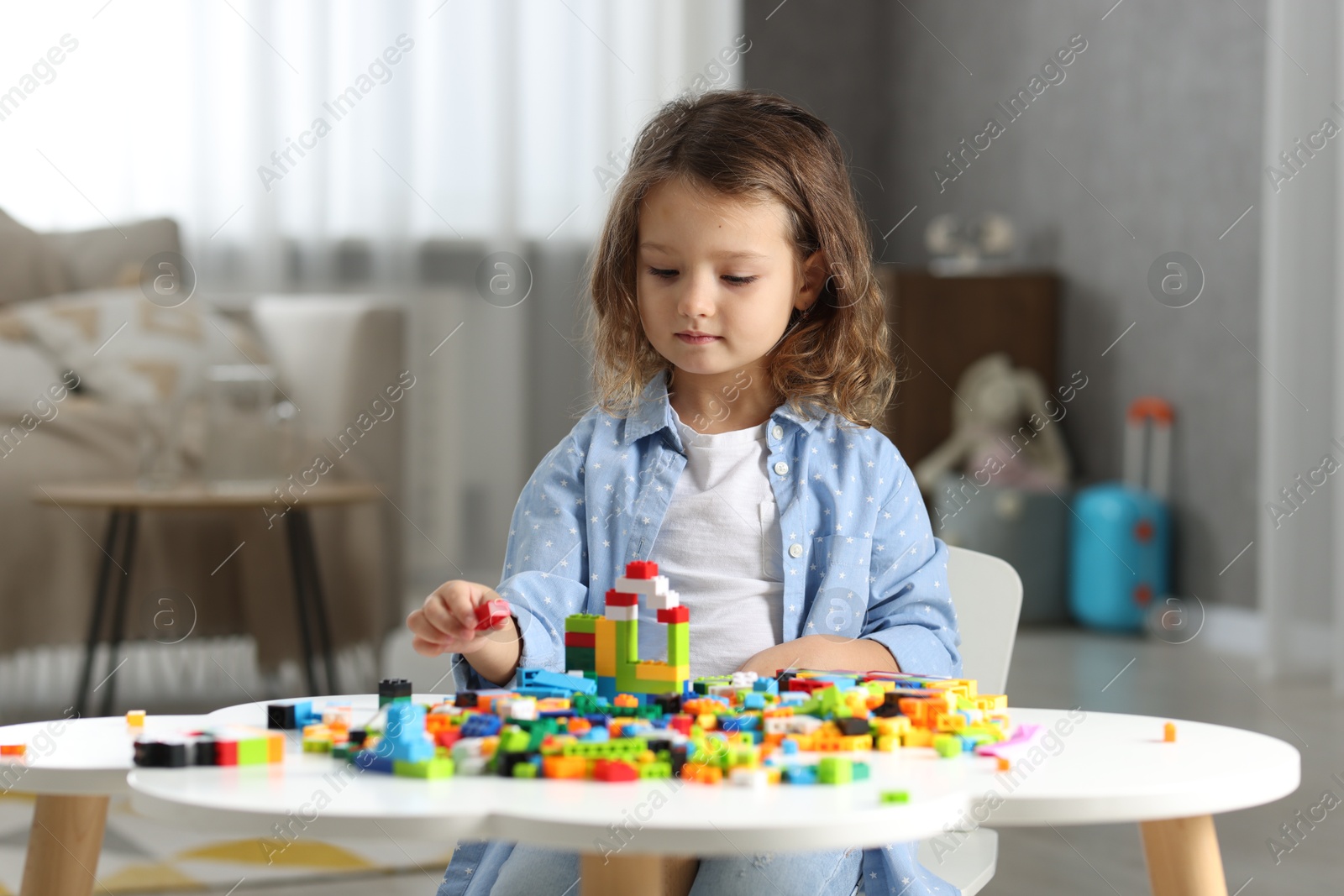 Photo of Cute girl playing with building blocks at white table indoors