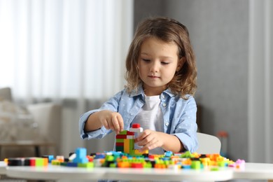 Photo of Cute girl playing with building blocks at white table indoors