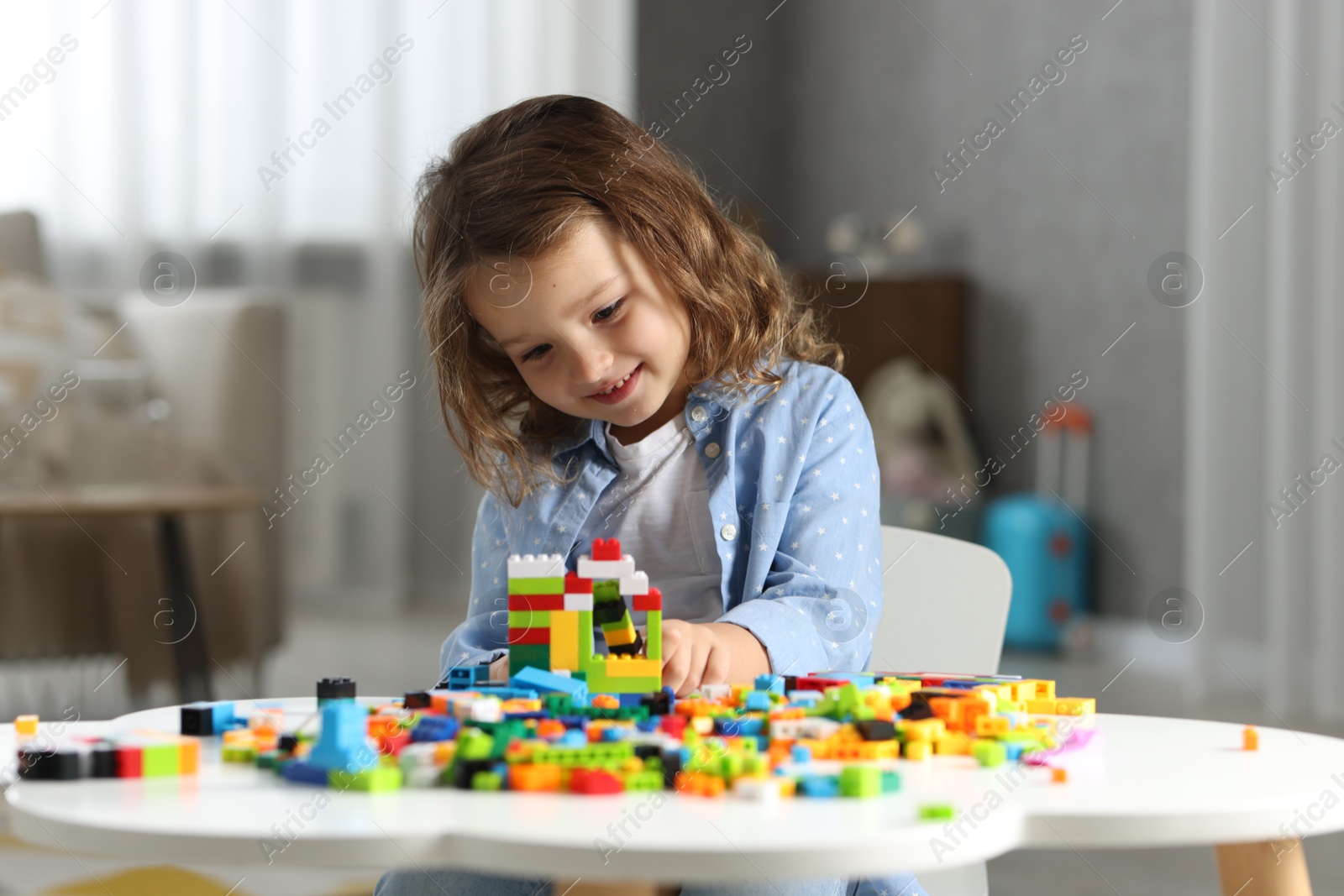 Photo of Cute girl playing with building blocks at white table indoors