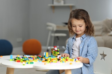 Photo of Cute girl playing with building blocks at white table indoors