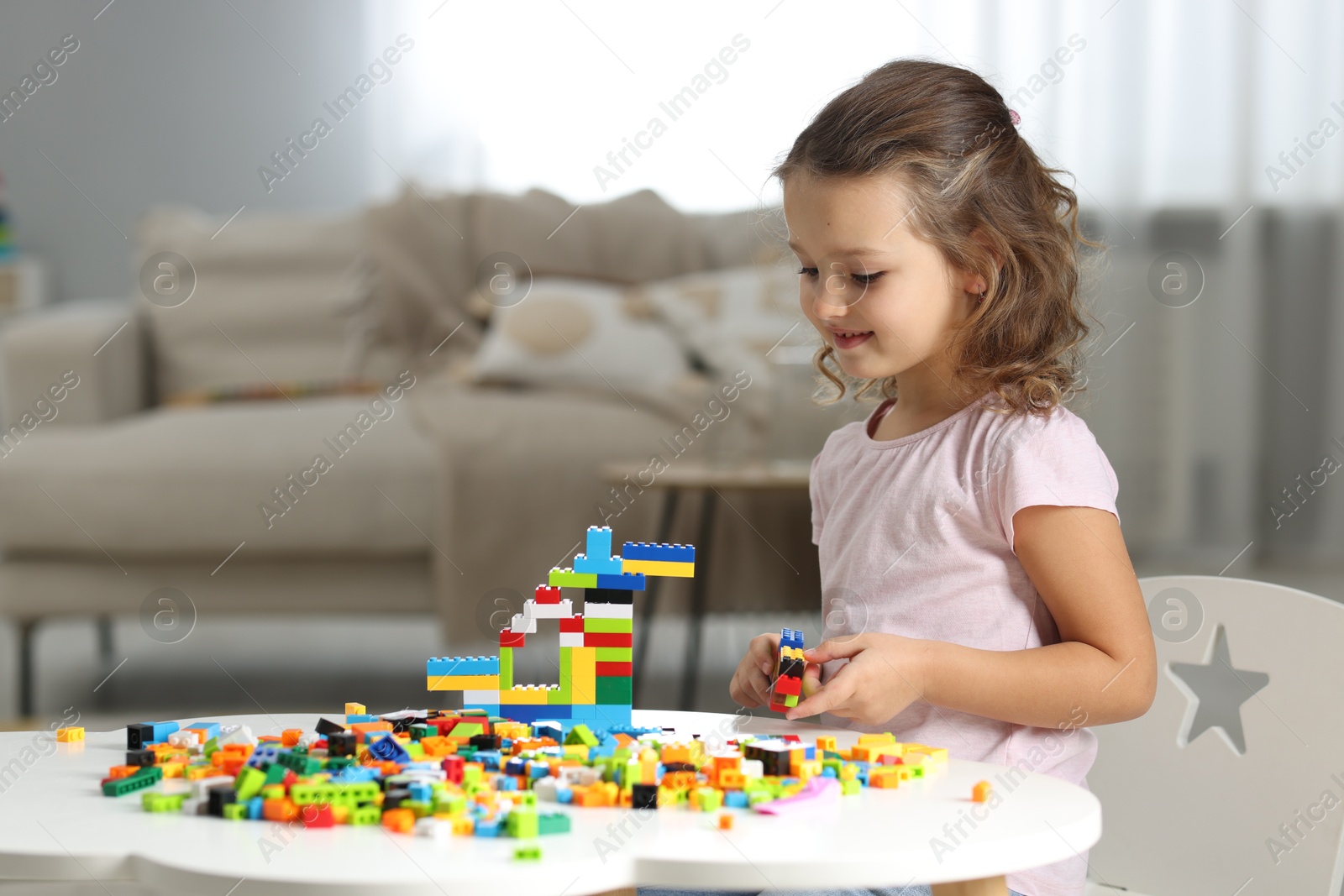 Photo of Cute girl playing with building blocks at white table indoors