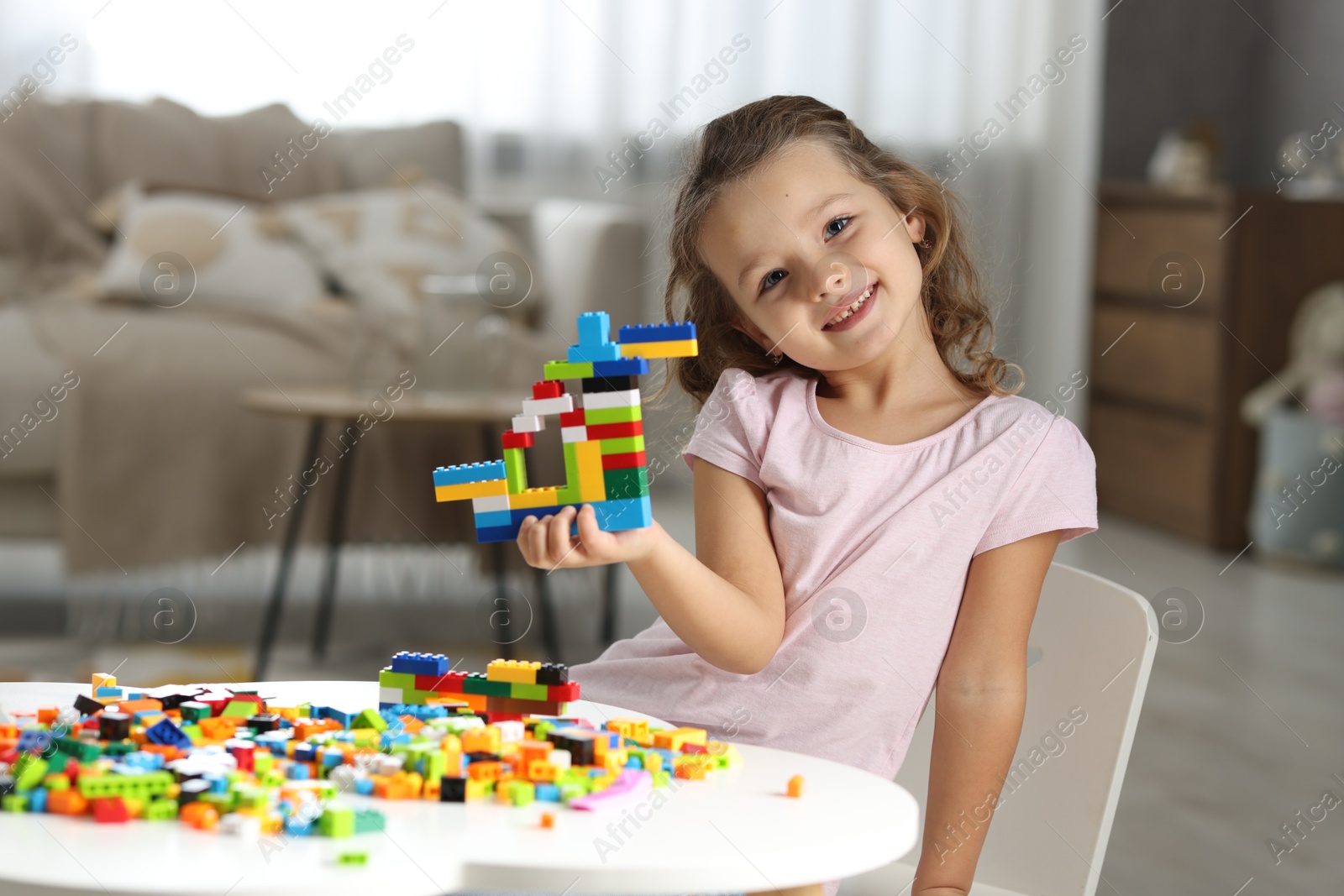 Photo of Cute girl playing with building blocks at white table indoors