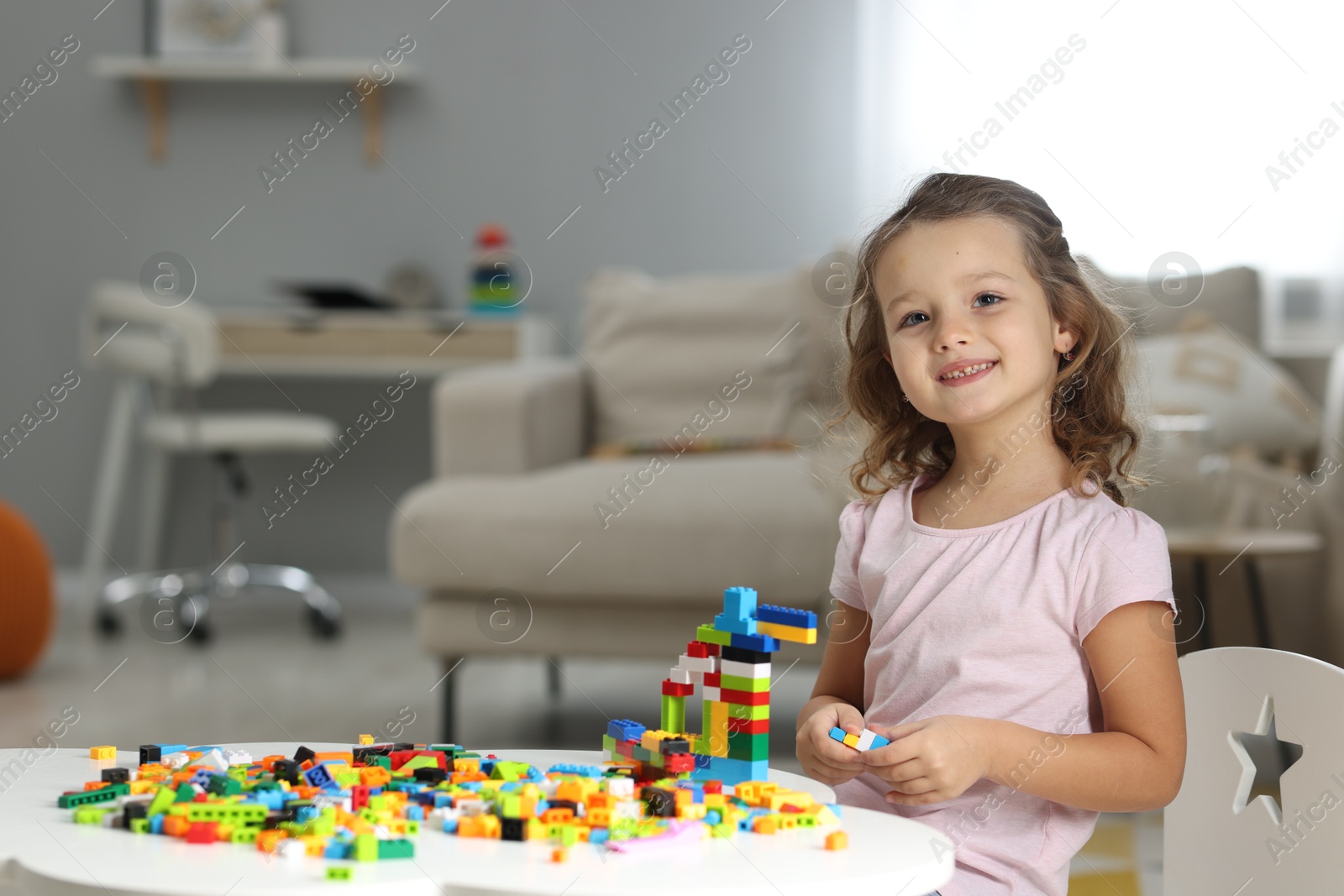 Photo of Cute girl playing with building blocks at white table indoors. Space for text