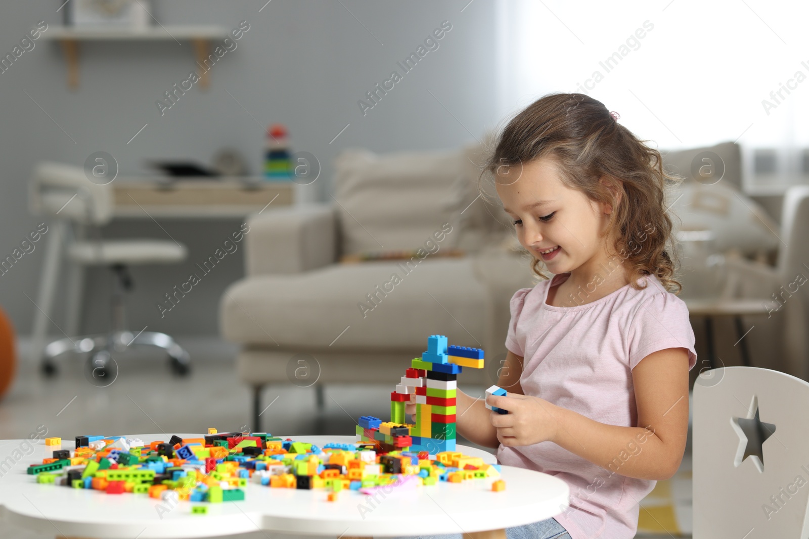 Photo of Cute girl playing with building blocks at white table indoors. Space for text