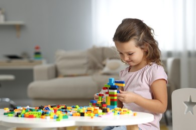 Photo of Cute girl playing with building blocks at white table indoors. Space for text