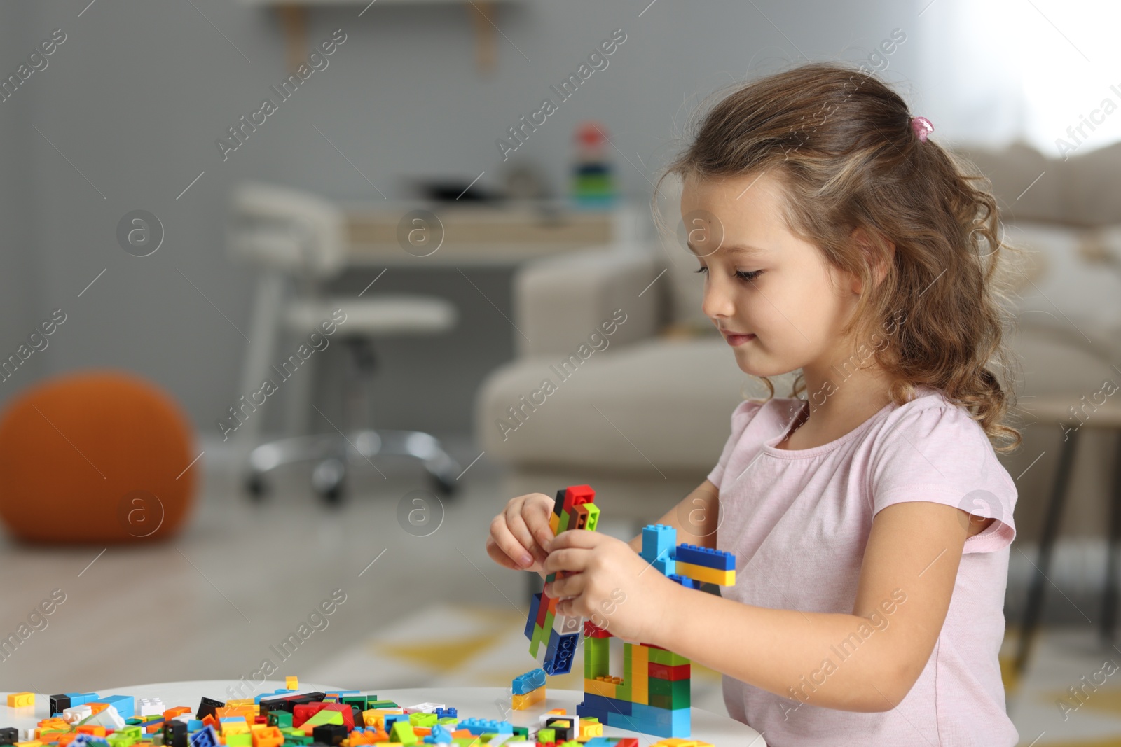 Photo of Cute girl playing with building blocks at white table indoors. Space for text