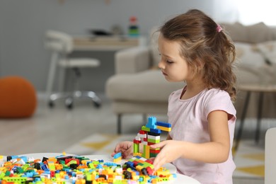 Photo of Cute girl playing with building blocks at white table indoors. Space for text