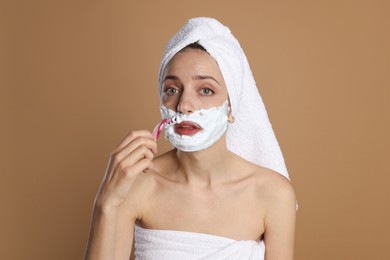 Photo of Beautiful woman shaving facial hair with razor on brown background