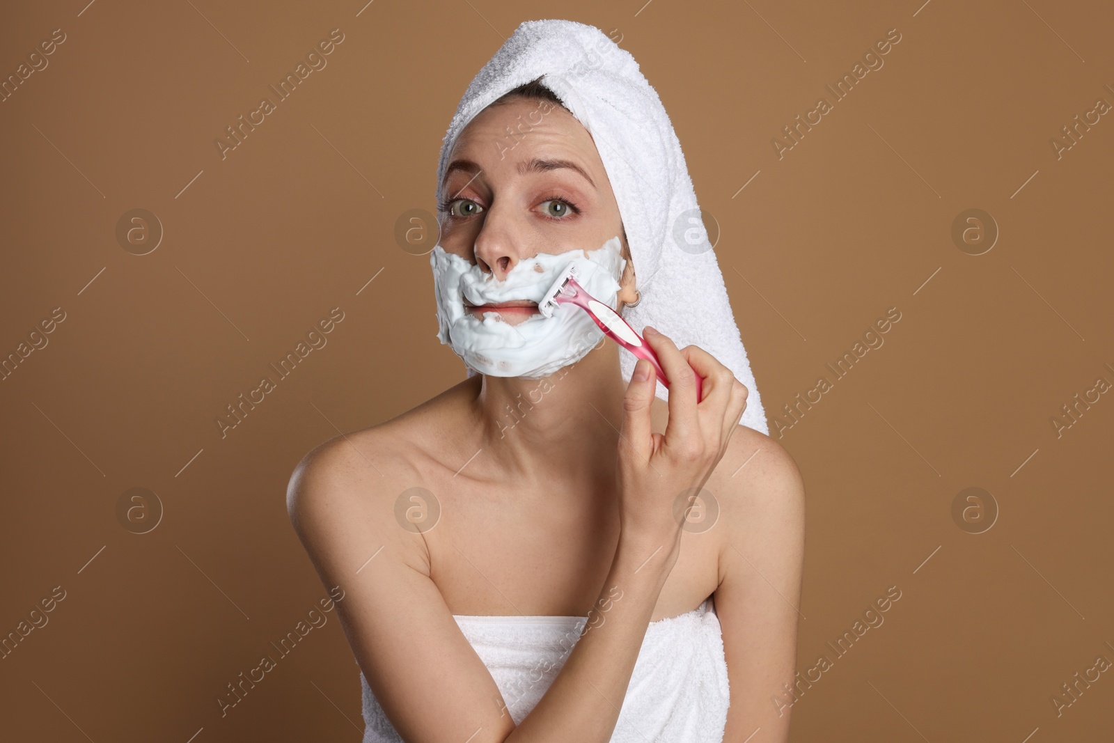 Photo of Funny woman shaving facial hair with razor on brown background