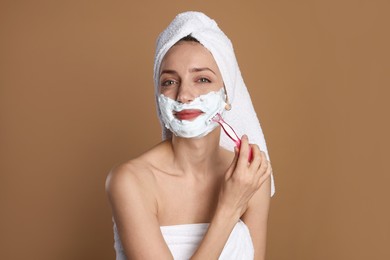 Photo of Funny woman shaving facial hair with razor on brown background