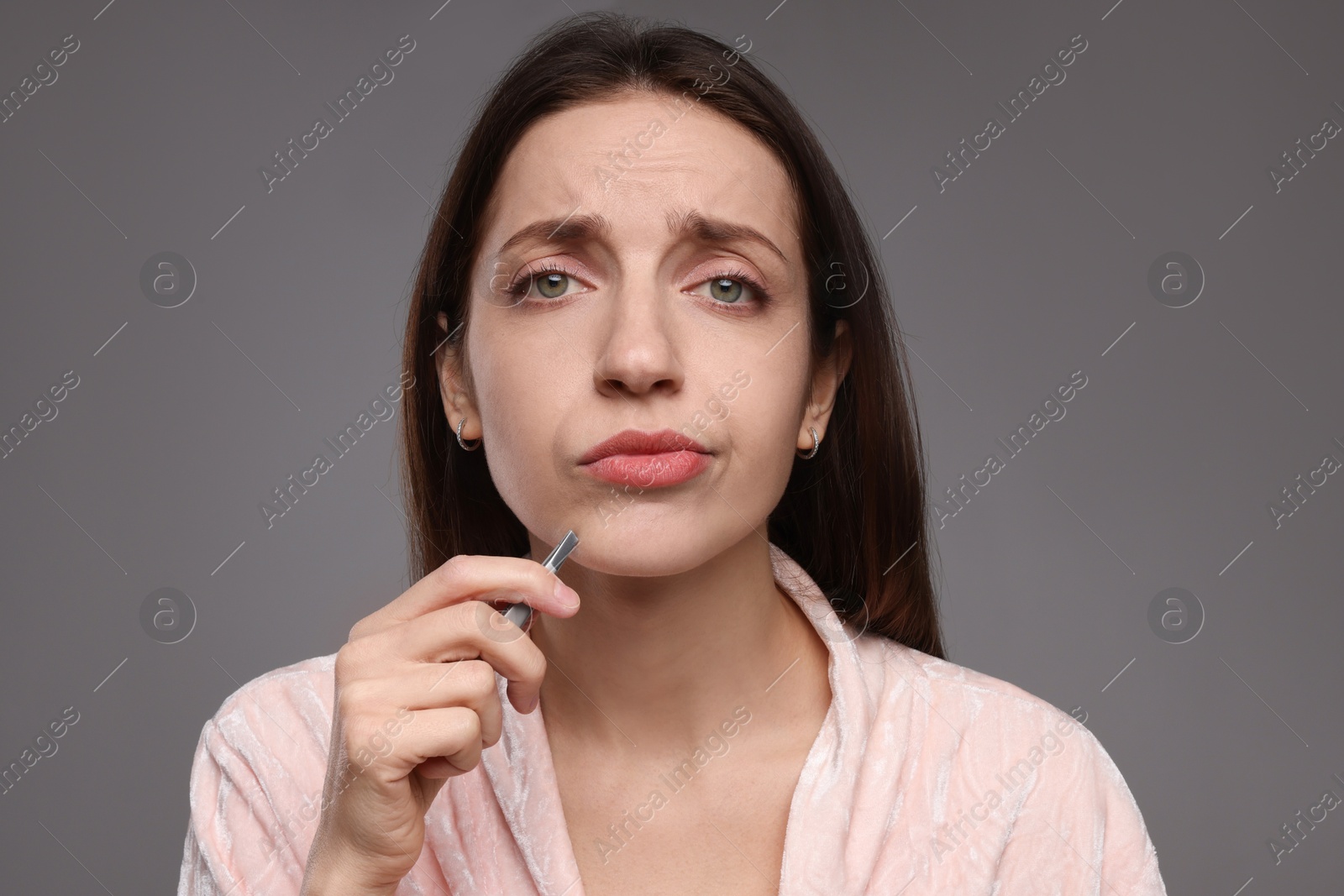 Photo of Beautiful woman plucking her mustache with tweezers on grey background