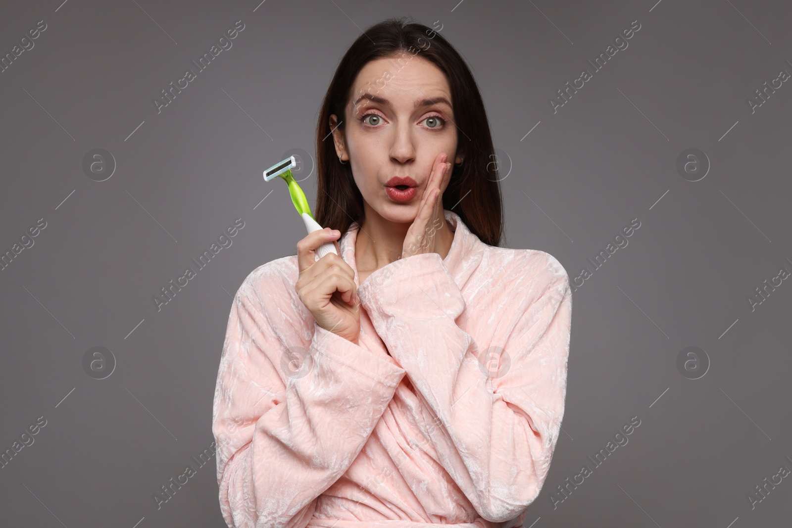 Photo of Surprised woman with razor on grey background. Hair removal tool