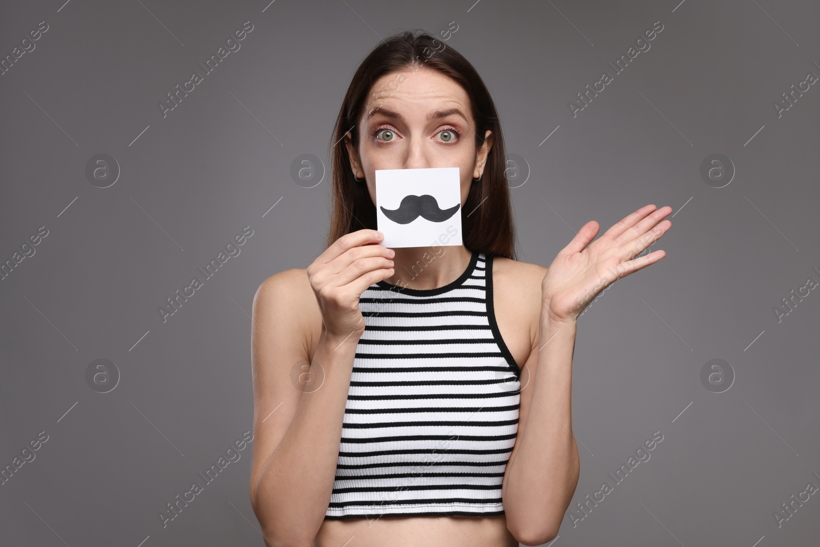 Photo of Woman holding paper with drawn mustache on grey background