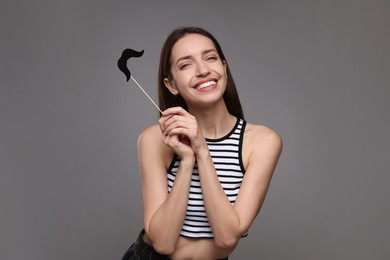 Smiling woman with fake paper mustache on grey background