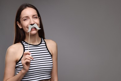 Photo of Smiling woman with fake paper mustache on grey background. Space for text